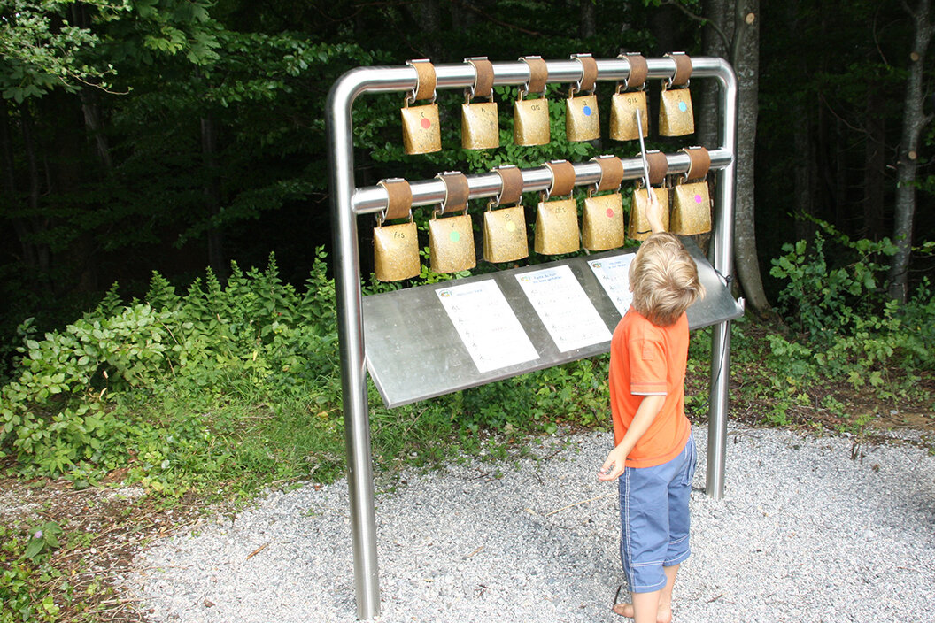 kleiner Junge der im Wald am Glockenspiel mit Kuhglocken beim Pfaffenwinkler Milchweg spielt